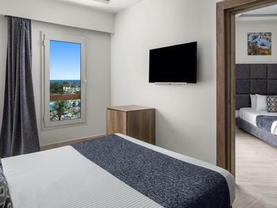 Chambre d'hôtel moderne avec lit double, TV murale et vue sur la ville par la fenêtre.