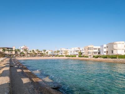 Coastline with clear water, beach chairs, and white hotels under a blue sky.