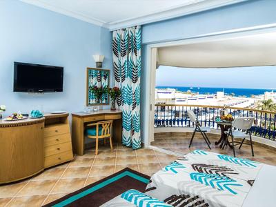 Hotelzimmer mit Balkon, Blick auf das Meer, Holzmöbel, TV und türkis-weiß gemusterte Textilien.