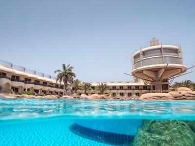Hotel with pool, palm trees, and a unique elevated round structure in a sunny setting.