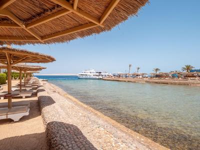 Beach with straw parasols and sunbeds along clear sea with yachts in the background