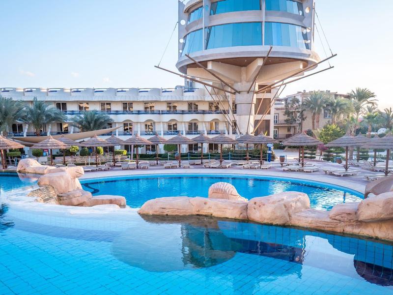 Hotel mit rundem Aussichtsturm und mehreren Pools im Außenbereich bei klarem Himmel.