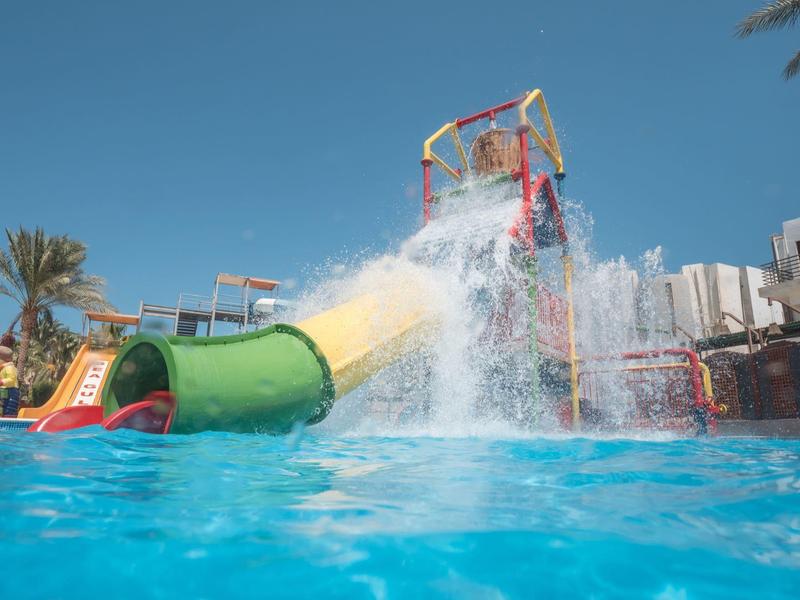 Hell eingerichtetes Hotelzimmer mit drei Betten, Balkon und Sitzbereich mit Tisch und Stühlen.