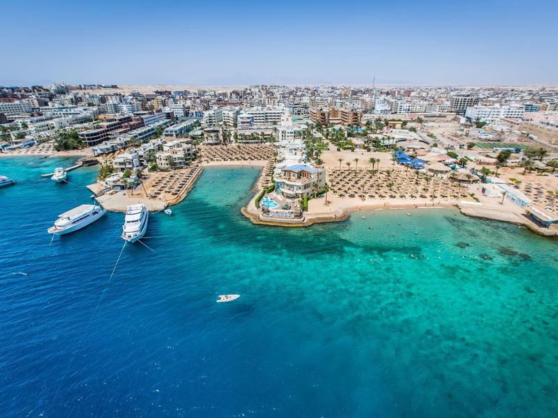 Klares Meer mit Booten, Sandstrände und Gebäude in einer sonnigen Küstenstadt.