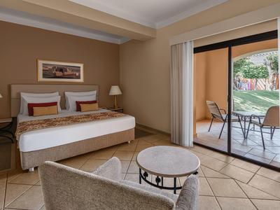 Cozy hotel room with double bed, seating area, and terrace overlooking garden.