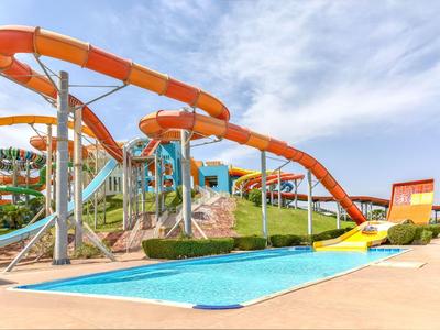 Grande toboggan aquatique avec des courbes orange au-dessus d'une piscine bleue sous un ciel ensoleillé.