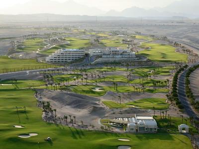Vue aérienne d'un hôtel avec un terrain de golf dans un paysage désertique avec des montagnes en arrière-plan.