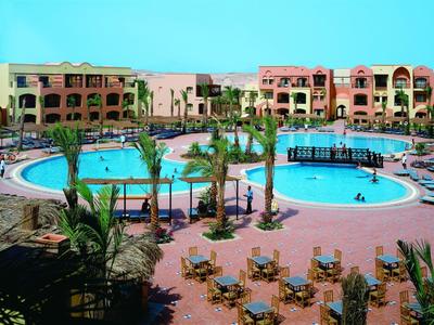 Large hotel pool with lounge chairs and palm trees, surrounded by multi-story buildings.