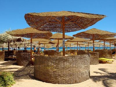 Strand met rieten parasols, zandgrond, blauwe lucht en oceaan op de achtergrond.