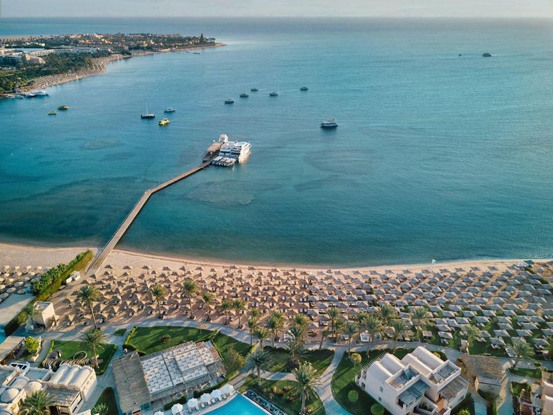 Aerial view of a beach with many sun loungers, umbrellas, and a long pier extending into the sea.