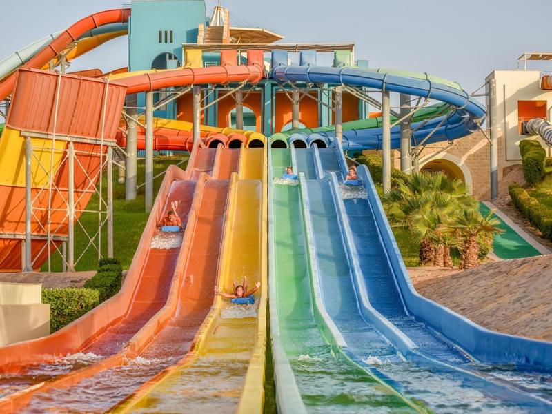 Colorful water slides in a water park with lounge chairs and buildings in the background.