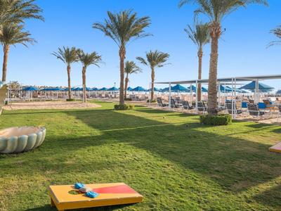 Green lawn with palm trees, beach loungers, and calm sea under a clear sky.