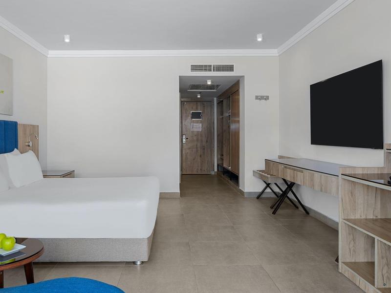 Modernes Hotelzimmer mit großem Bett, Flachbildfernseher und schlichtem, hellem Interieur.