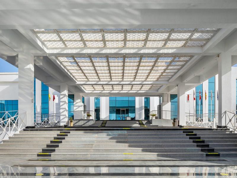 Moderner Eingangsbereich mit breiter Treppe und Glasüberdachung bei klarem Himmel.