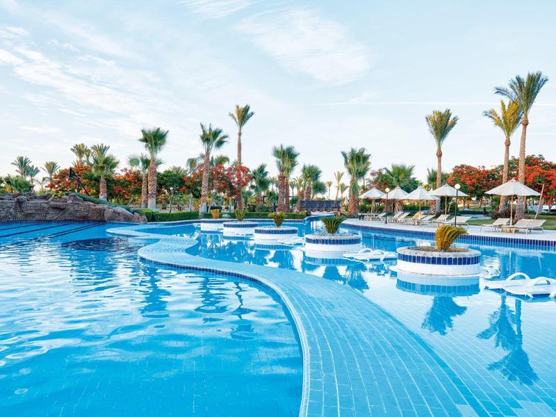Large blue pool with sun umbrellas and palm trees under a blue sky