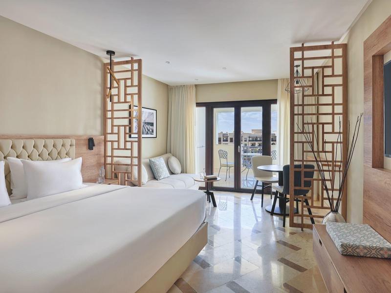 Elegant hotel room with large bed, stylish partitions, and balcony with a view.