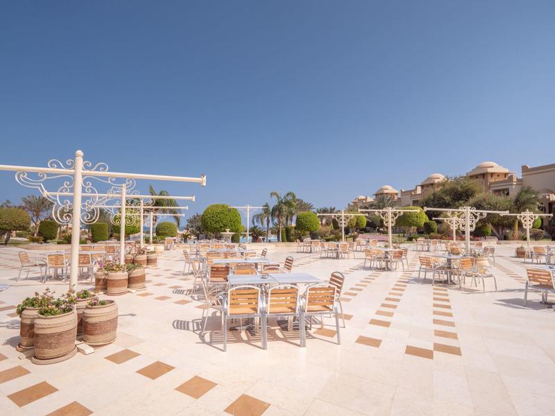 Weitläufige Terrasse mit leeren Tischen, Stühlen, blauen Himmel und Hügelhäuser im Hintergrund.