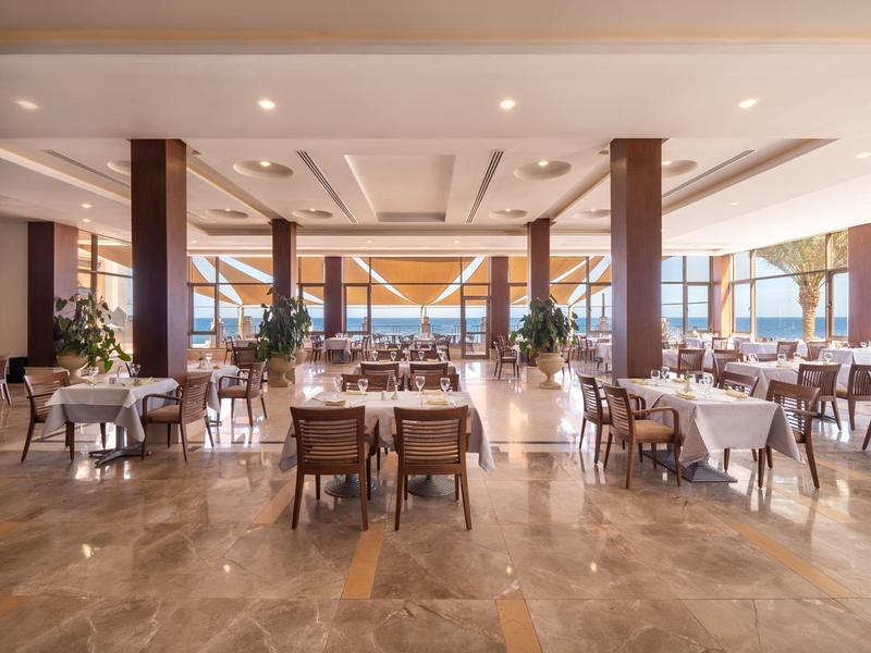 Großer, heller Speisesaal mit weißen Tischdecken, Holzmöbeln und großen Fenstern mit Außenblick.