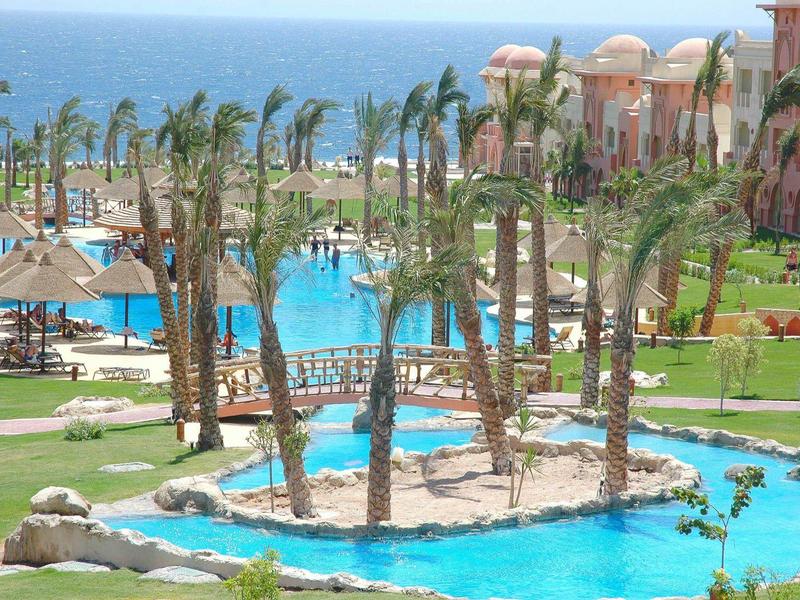 Kleines Bad mit weißer Toilette, eckigem Waschbecken, großem Spiegel und beige-grauen Fliesen.