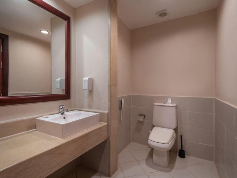 Kleines Bad mit weißer Toilette, eckigem Waschbecken, großem Spiegel und beige-grauen Fliesen.