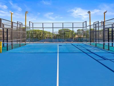 Niebieskie korty tenisowe z otaczającą siatką pod czystym, niebieskim niebem na zewnątrz.