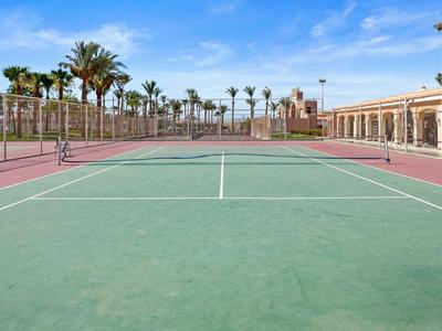 Otwarty kort tenisowy z palmami i niebieskim niebem w tle.