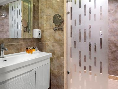 Modernes Badezimmer mit weißem Waschbecken, braunen Fliesen und halbtransparentem Duschvorhang.