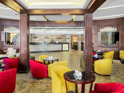 Modernes Café mit rot-gelben Sesseln, Holztischen, Steinsäulen und heller Deckenbeleuchtung.