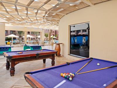 Zwei Billardtische mit blauem Tuch stehen in einem überdachten, hellen Raum mit offenem Zugang.