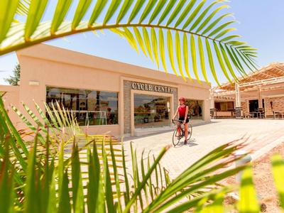 Vstup do hotelu se slunečním svitem a cyklistou, v popředí palmové listy.