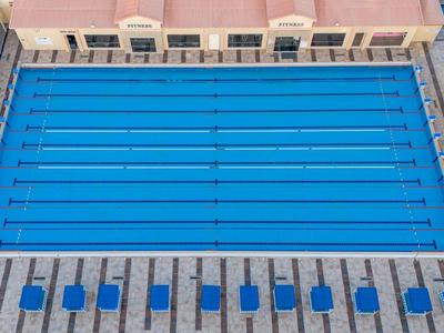 Widok z góry na prostokątny basen z niebieskimi leżakami na brzegu.