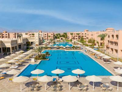 Duży basen hotelowy z leżakami i parasolami pod niebieskim niebem.