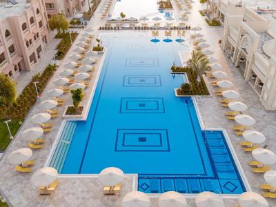 Duży prostokątny basen z białymi parasolami i leżakami w ośrodku hotelowym.