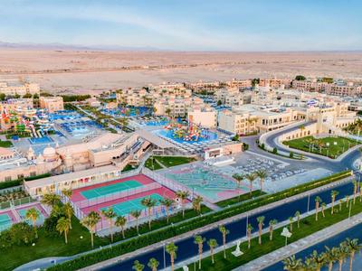 Widok na rozległy kompleks hotelowy z basenami, kortami tenisowymi i pustynnym krajobrazem w tle.