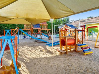 Kolorowy plac zabaw dla dzieci z piaskową nawierzchnią oraz różnymi urządzeniami do wspinaczki i zjeżdżania pod parasolami.