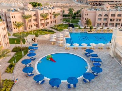 Widok na kurort z wieloma basenami, otaczającymi budynkami i niebieskimi parasolami.