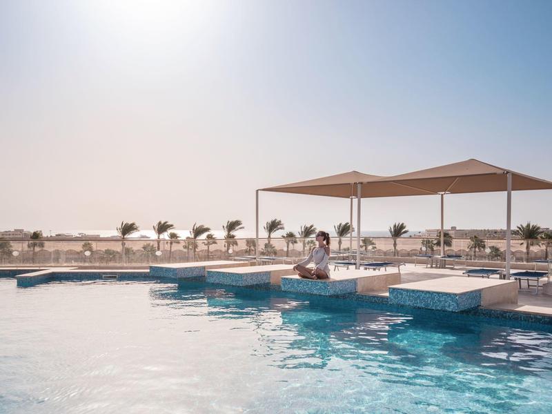 Ein großer Outdoor-Pool mit klarem Wasser, Sonnensegeln und Liegestühlen unter hellem Himmel.