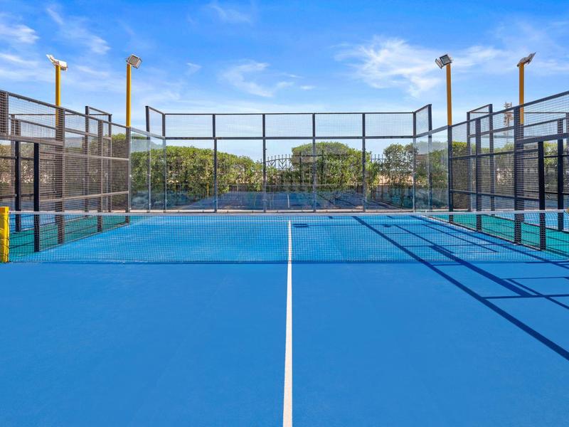 Freier blauer Paddle-Tennisplatz mit Netzen, Zäunen und strahlend blauem Himmel.