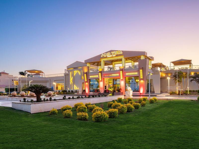 Großes, beleuchtetes Gebäude mit Terrasse und gepflegtem Garten bei klarem Himmel.