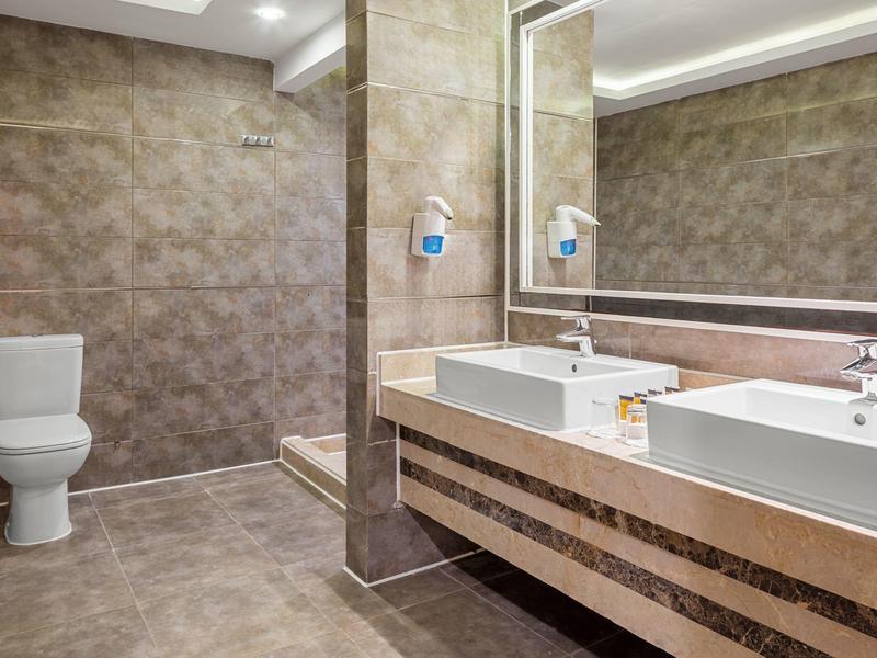 Modernes Bad mit Wandtoilette, Doppelwaschbecken, großem Spiegel und braunen Fliesen.