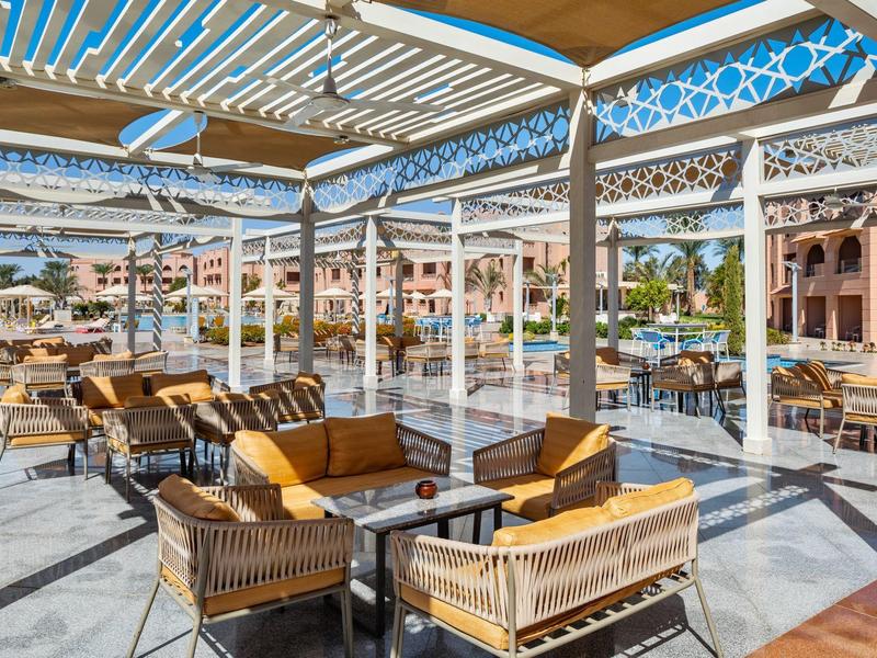 Offener Terrasse mit Pergola, Korbmöbeln und Blick auf Pool und mediterrane Häuser.