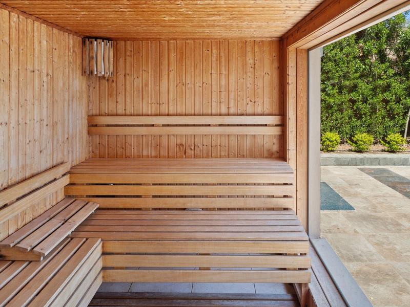 Helle Holzsauna mit mehrstufigen Bänken und Fenster mit Blick auf bewachsenen Außenbereich.