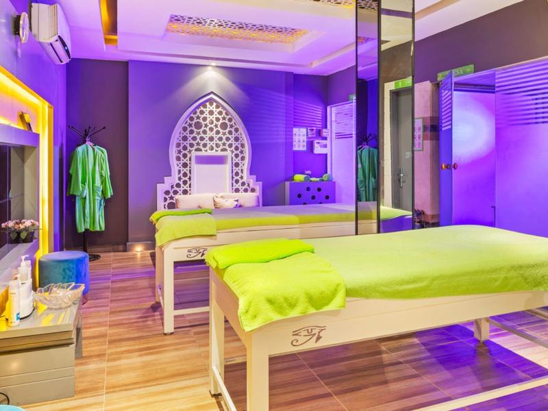 Ein farbenfrohes Wellnesszimmer mit lila Wänden, grünen Handtüchern und zwei Massageliegen.