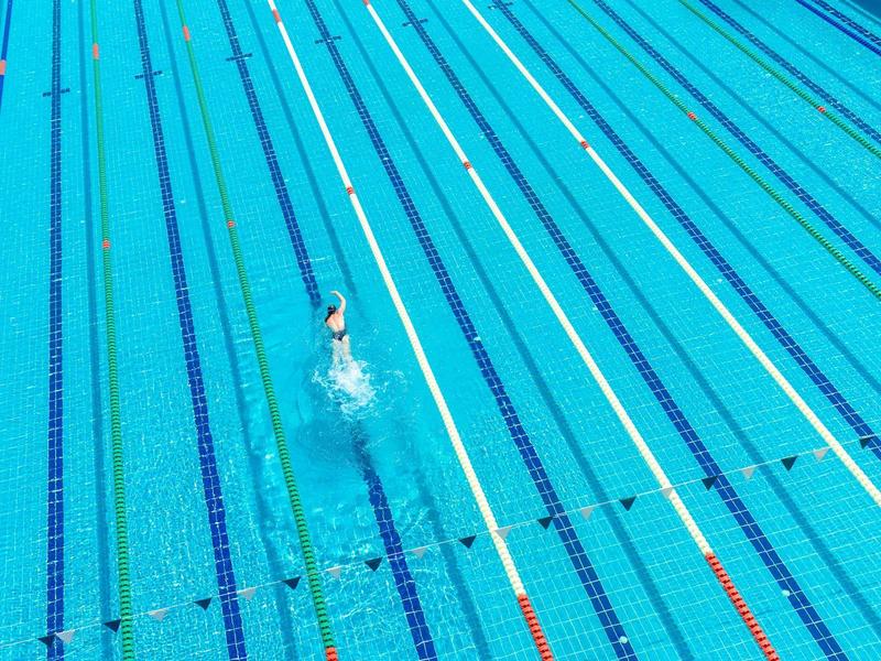 Leeres Schwimmbecken mit einer Person, die auf der Bahnmitte schwimmt, und blauen Wasserlinsen.