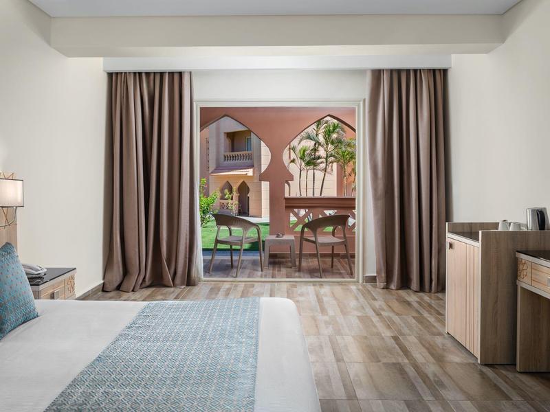 Helles Schlafzimmer mit großem Bett, Holzboden und Zugang zu Terrasse mit Tisch und Stühlen.