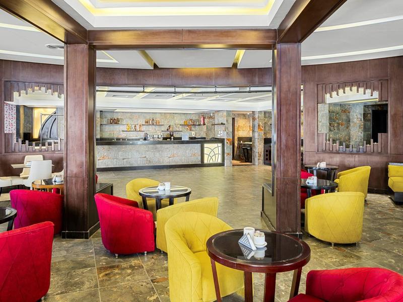 Modernes Café mit rot-gelben Sesseln, Holztischen, Steinsäulen und heller Deckenbeleuchtung.