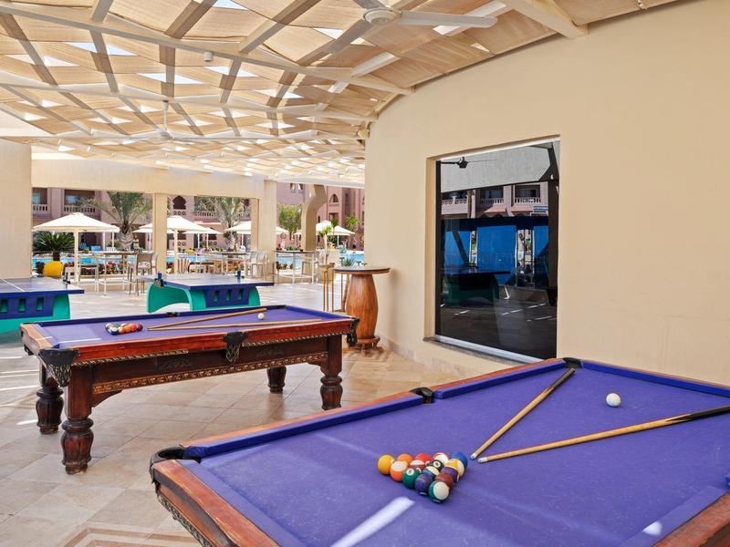 Zwei Billardtische mit blauem Tuch stehen in einem überdachten, hellen Raum mit offenem Zugang.