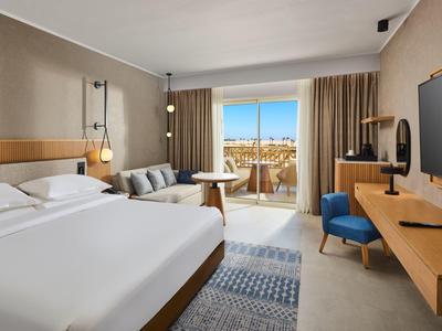 Modernes Hotelzimmer mit großem Bett, Sofa, Balkon und Fernsehgerät an der Wand.