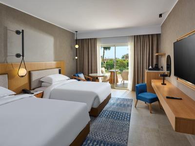 Modernes Hotelzimmer mit zwei großen Betten, Holzmöbeln, Teppichboden und Balkon mit Aussicht.