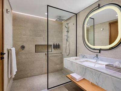 Moderner, heller Badezimmerraum mit begehbarer Dusche, rundem beleuchtetem Spiegel und Marmorwaschbecken.